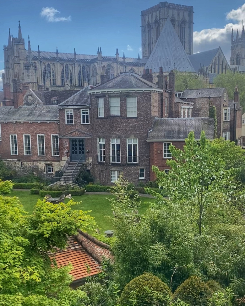 A view of the York Minster, with an old red brick building with a garden in front