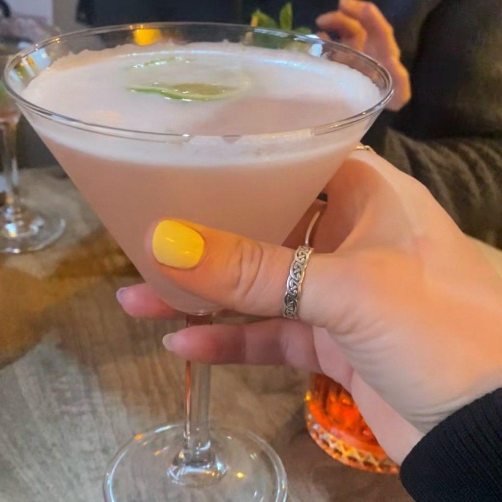 A pink cocktail with a slice of lime