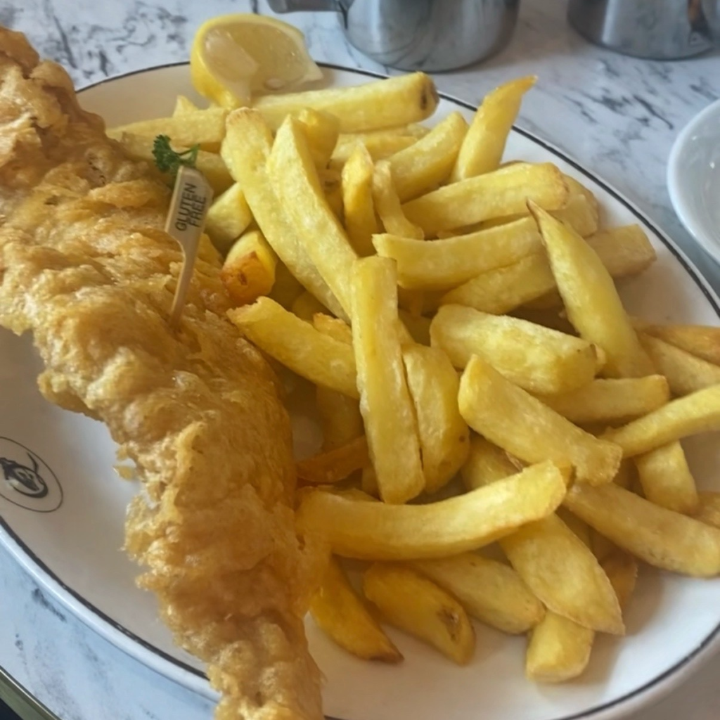 A close up of battered fish and chips, with a wooden tab labelling the fish as gluten free.