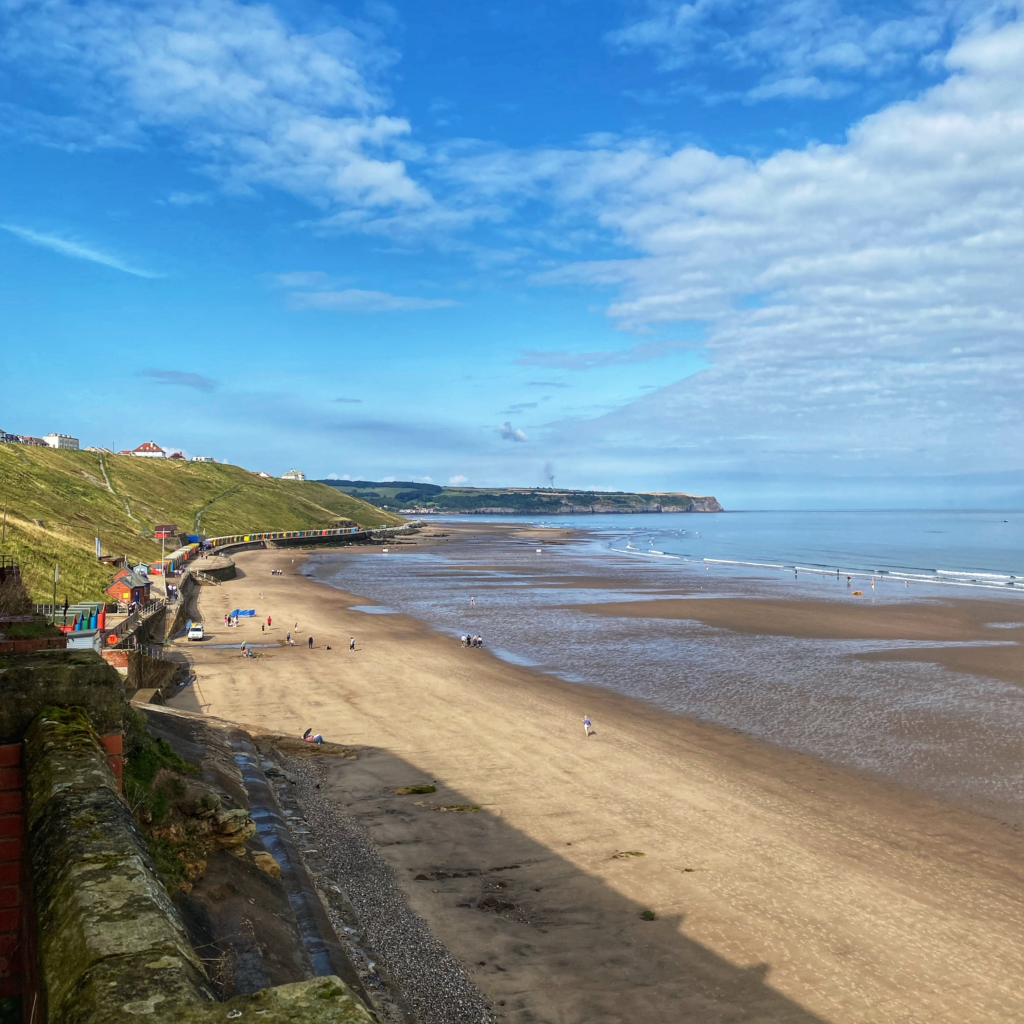 The sandy Whitby beach and coastline, with a blue sunny sky. 