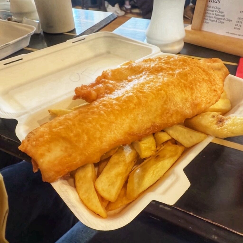 A close up of battered fish placed on top of golden chips in a plastic box