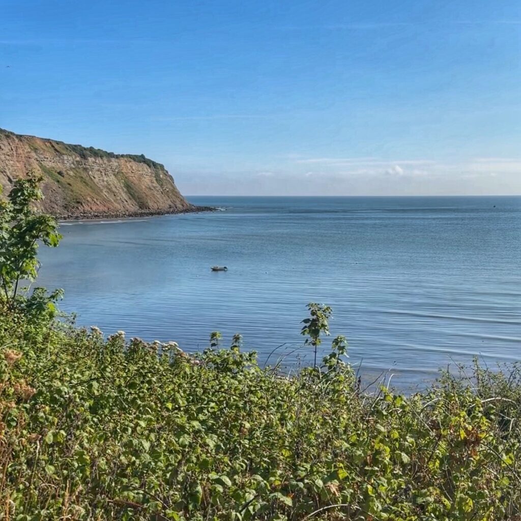 The view of the bright blue sea with the cliffside in the background