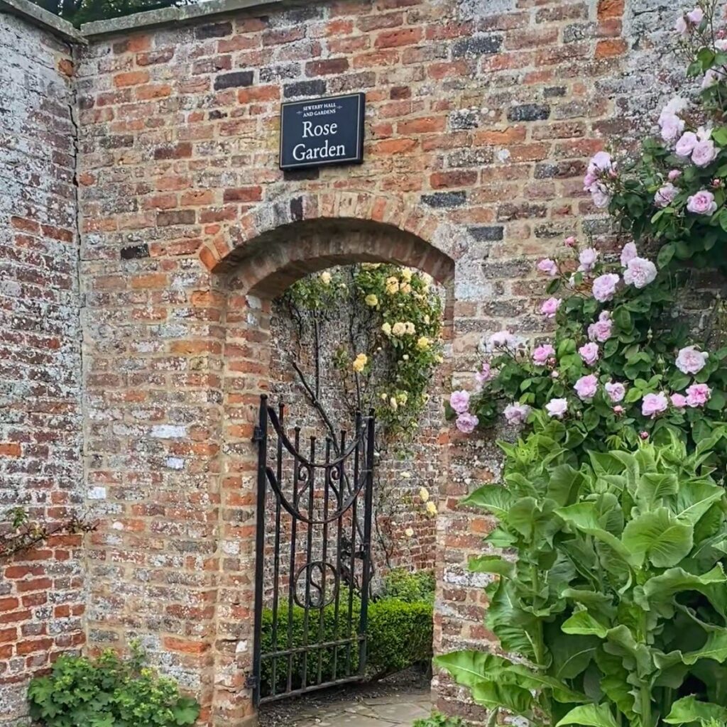 A brick wall with a doorway, with the sign 'Rose garden' above
