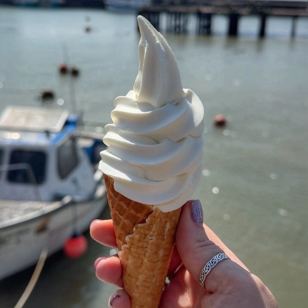 A white soft serve ice cream cone with a white boat in the background