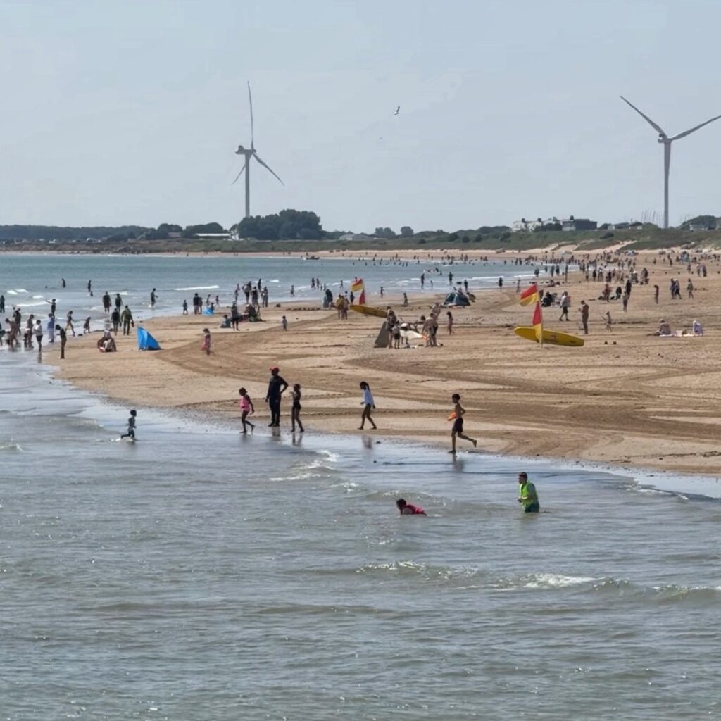 A yellow sandy beach with families playing in the sea